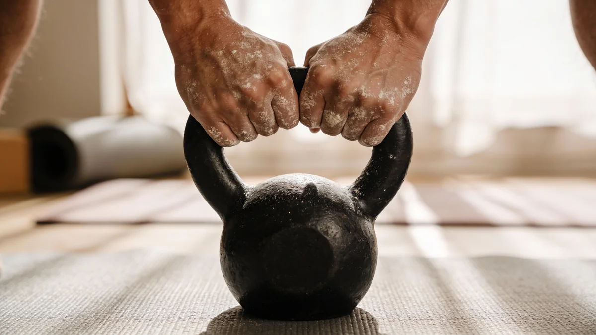 Manos agarrando el asa de una kettlebell de hierro fundido para elegir el peso adecuado
