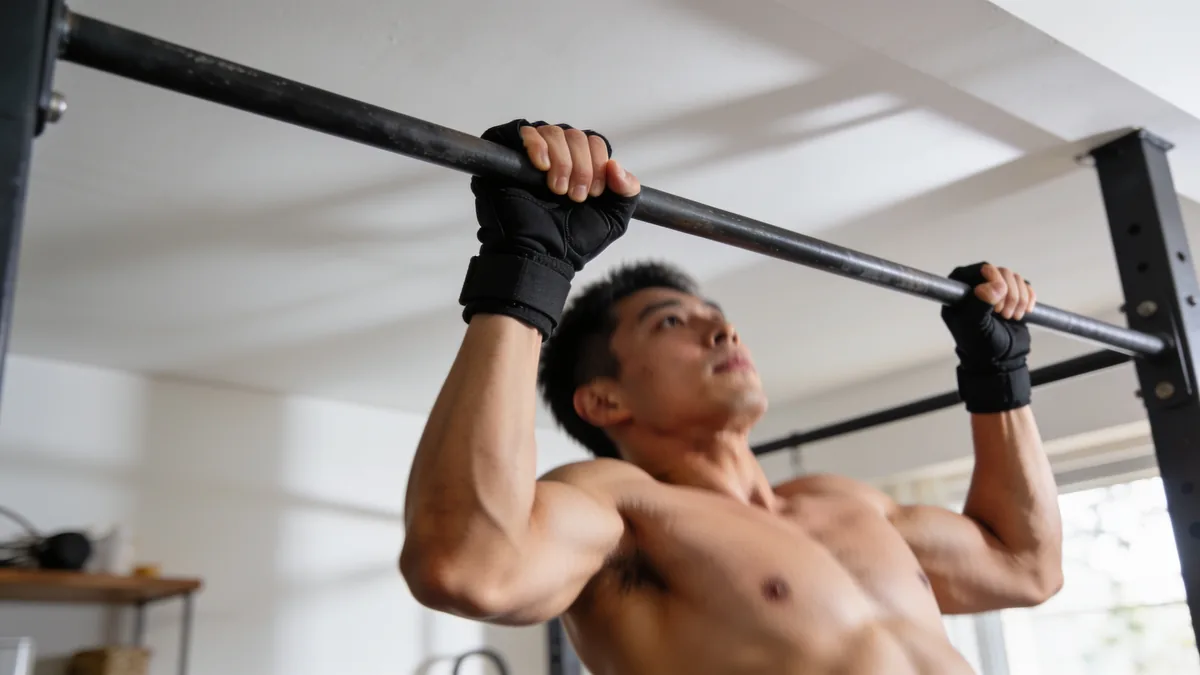 Hombre haciendo dominadas con guantes de gimnasio con soporte de muñeca