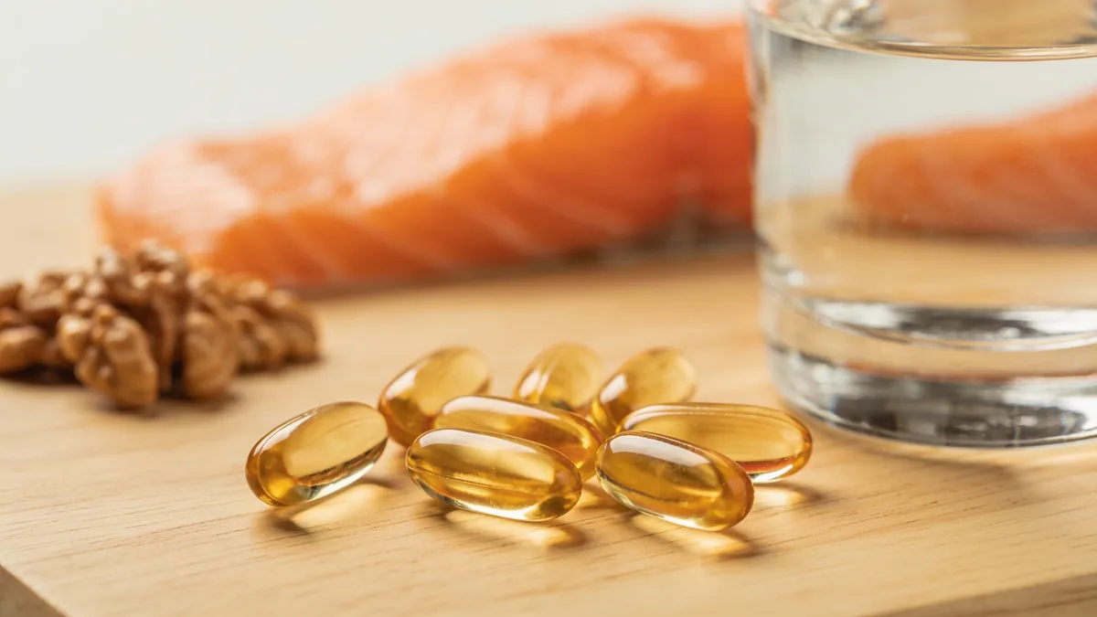 Cápsulas de omega 3 sobre mesa de madera junto a salmón y nueces, suplemento OMEGOR Vitality 1000